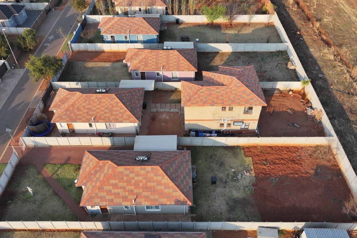 Aerial view of a residential estate showing multiple detached houses with tiled roofs, enclosed by precast concrete boundary walls and featuring paved driveways.