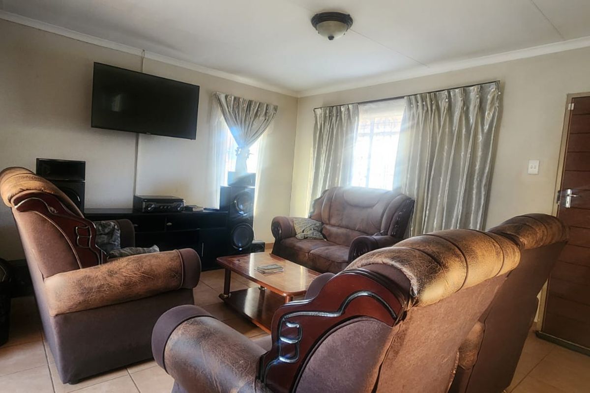 A functional living room featuring tiled flooring, neutral wall finishes, and a wooden entrance door, providing a comfortable and practical living space.
