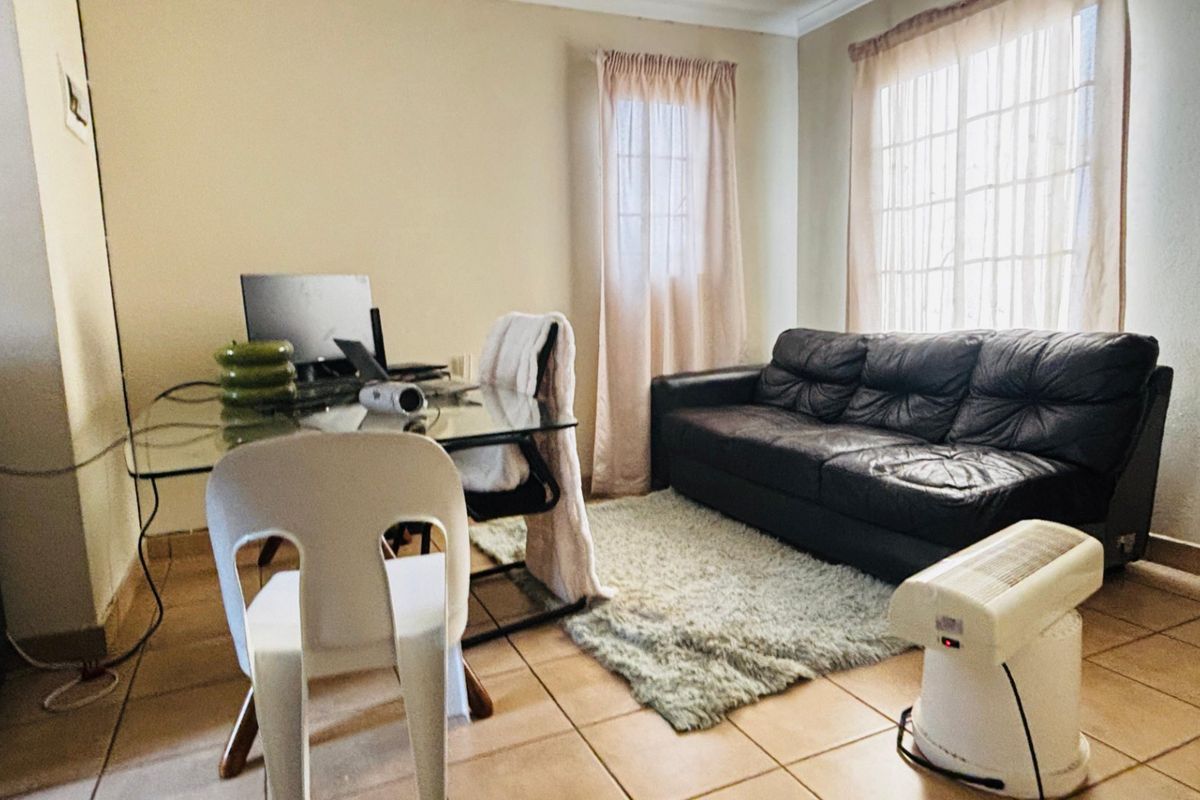A functional living room space featuring tiled flooring and natural light from the windows, suitable for a comfortable lounge or home office setup.