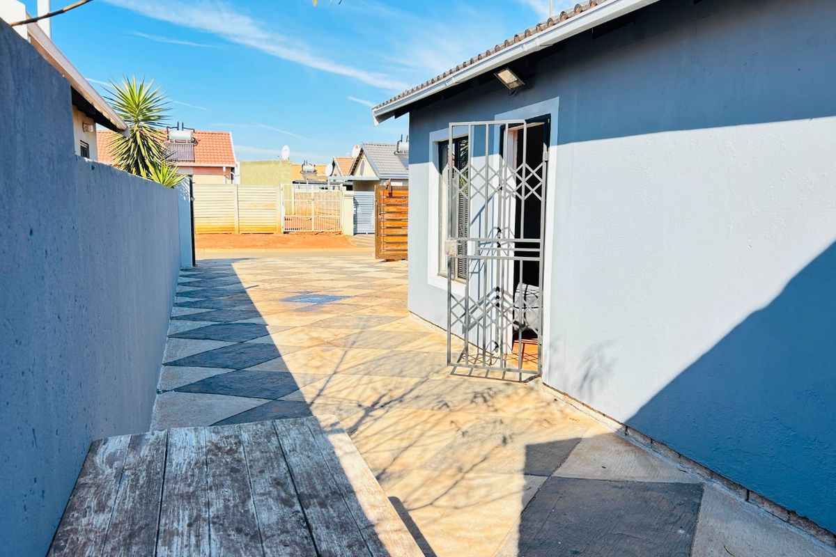 A paved rear courtyard area featuring a security gate entrance and boundary wall, providing a functional outdoor space.