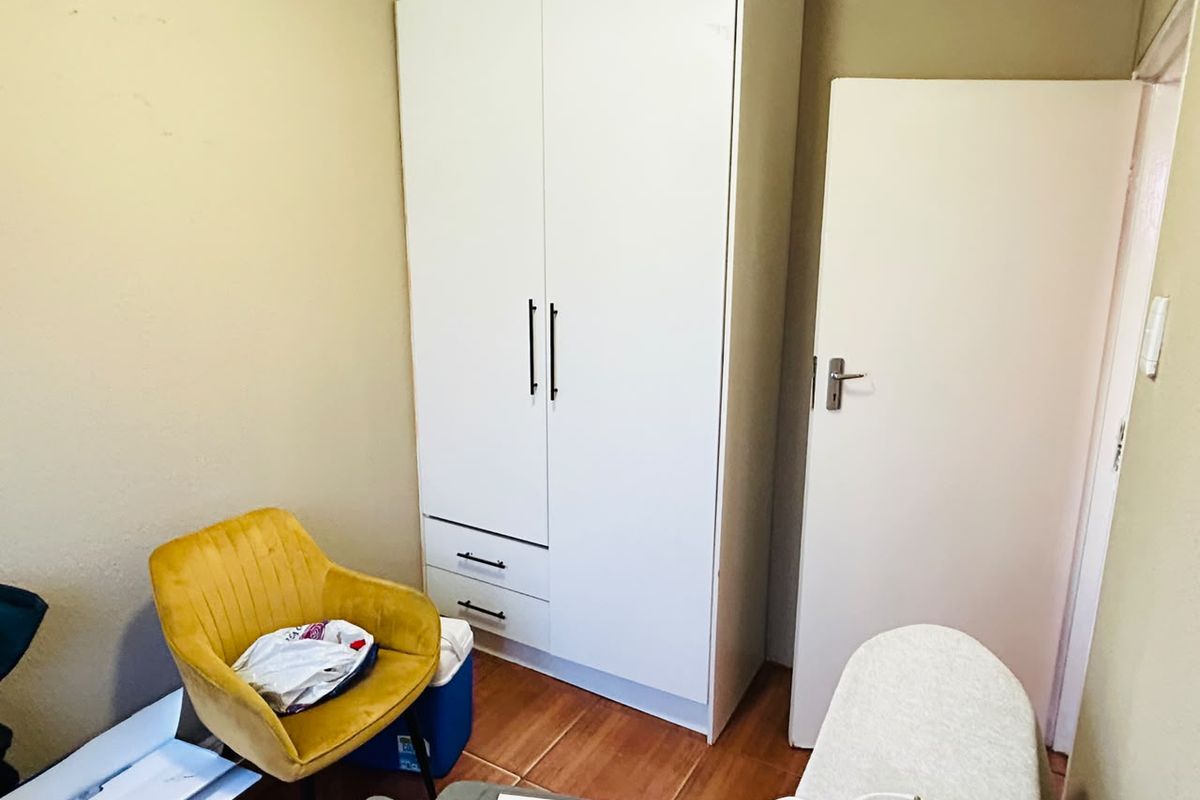 A bedroom featuring a modern white built-in wardrobe and tiled flooring, offering a functional storage solution.