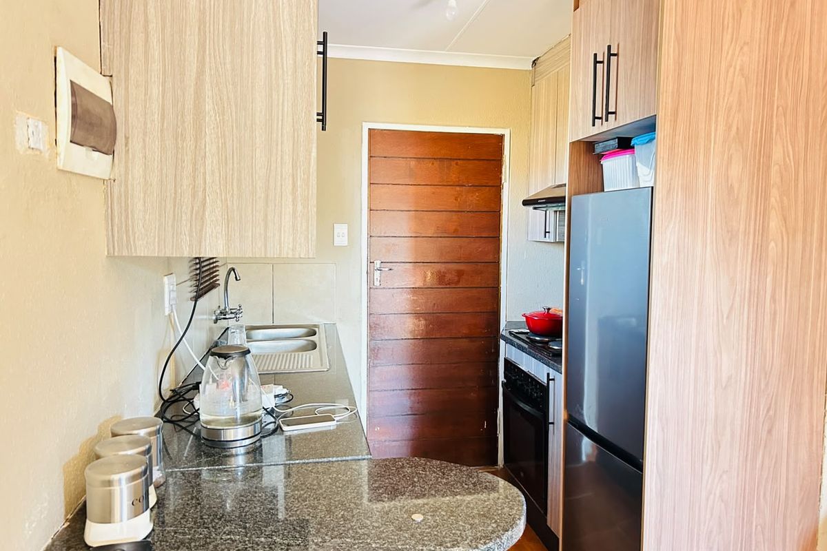 Compact kitchen featuring granite countertops, built-in cabinetry, and integrated cooking appliances, providing a functional workspace with direct access to an exterior door.