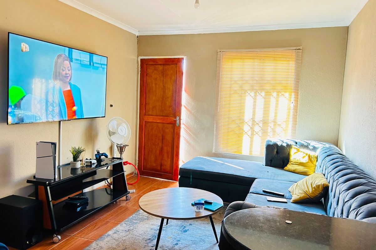 A comfortable living room featuring tiled flooring, a timber entrance door, and venetian blinds, providing a functional and well-lit space for relaxation.