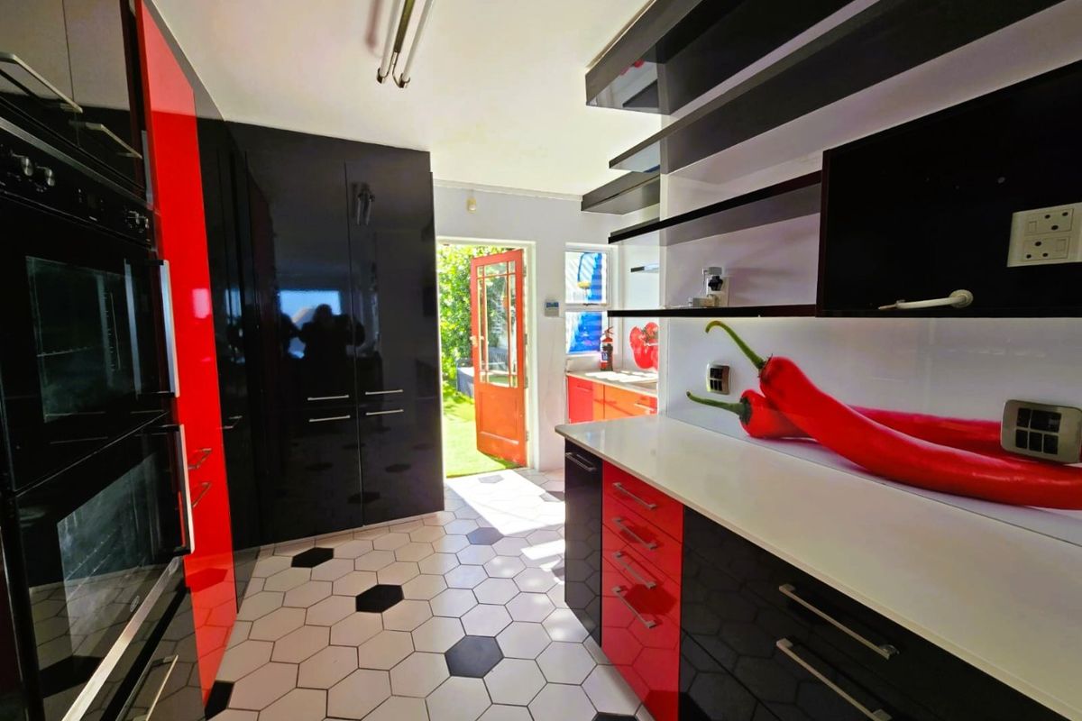 Modern kitchen featuring high-gloss black and red cabinetry, white countertops, hexagonal floor tiles, and direct access to the rear garden.