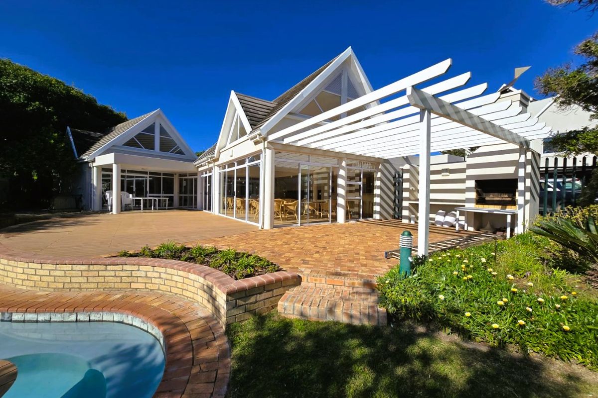 Rear exterior view featuring a swimming pool, brick paved patio, pergola, and built-in braai area with large glass sliding doors leading into the home.