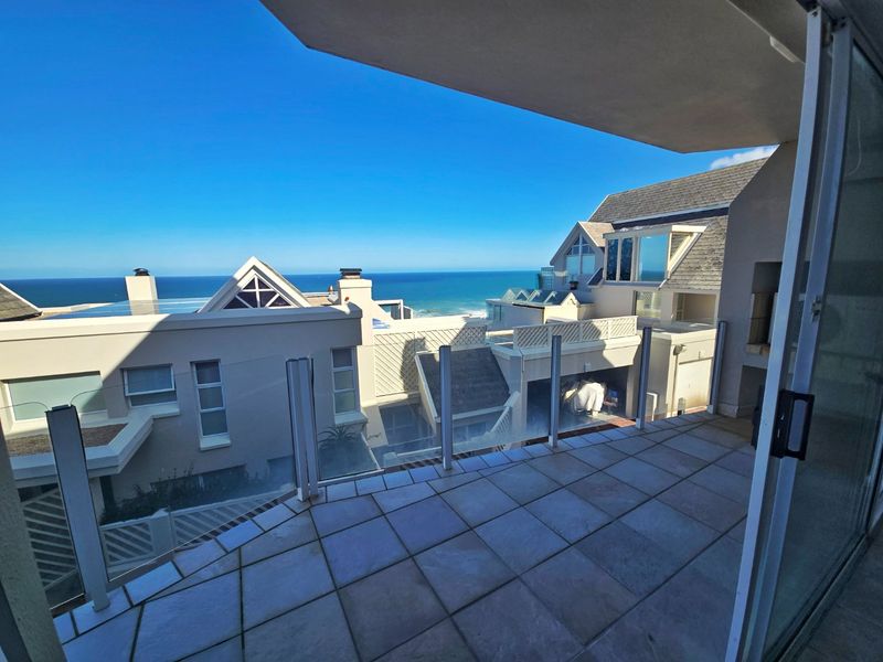 A spacious balcony featuring tiled flooring and a modern glass balustrade, offering expansive ocean views and overlooking the surrounding townhouse complex.