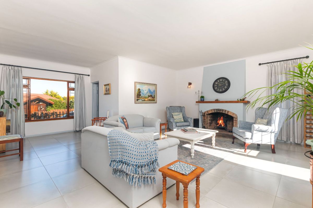 A bright and spacious living room featuring a classic brick fireplace with a wooden mantelpiece and large windows providing natural light.