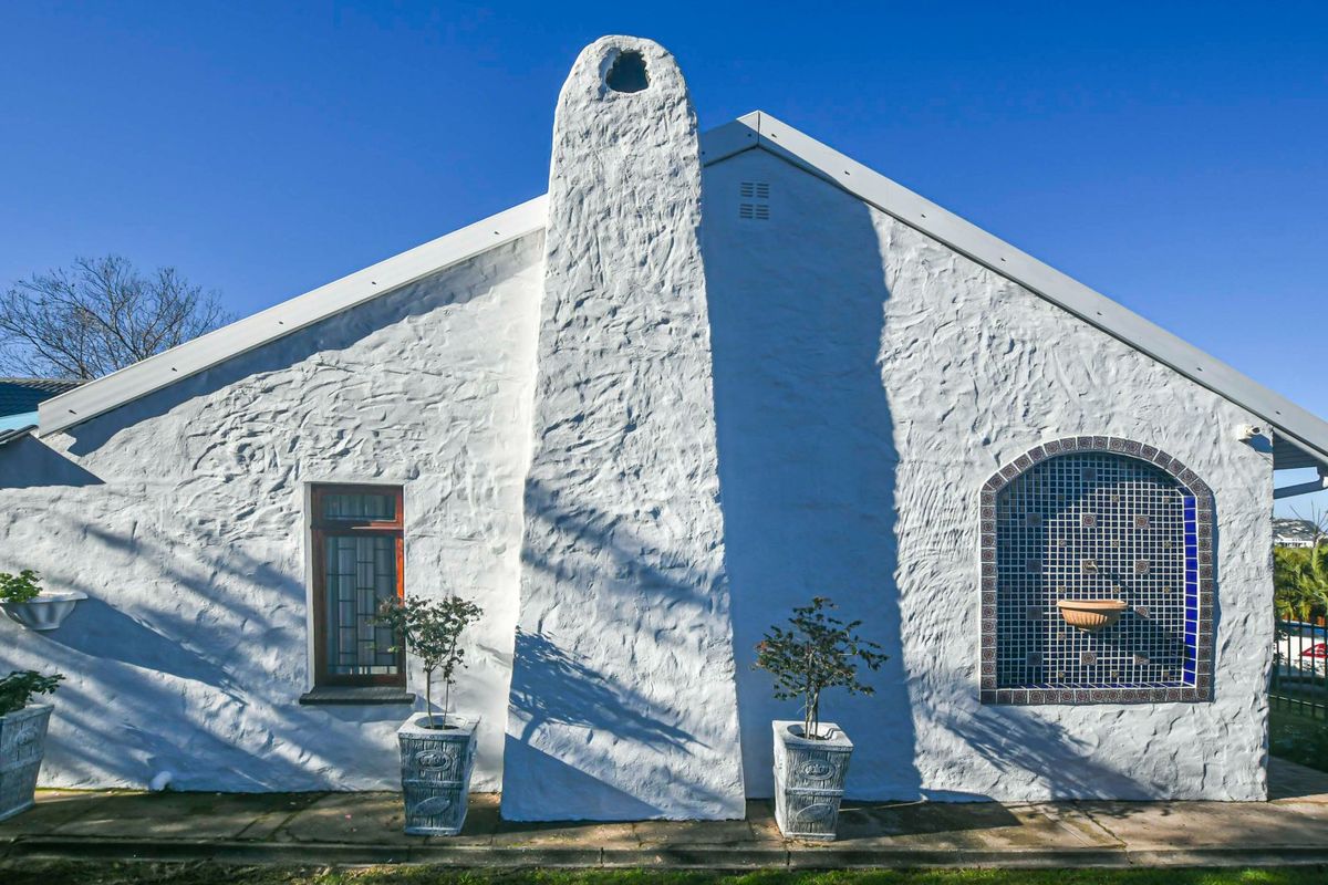 A well-maintained rear exterior elevation featuring a distinctive textured white masonry wall, a prominent chimney stack, and a decorative arched tiled water feature.