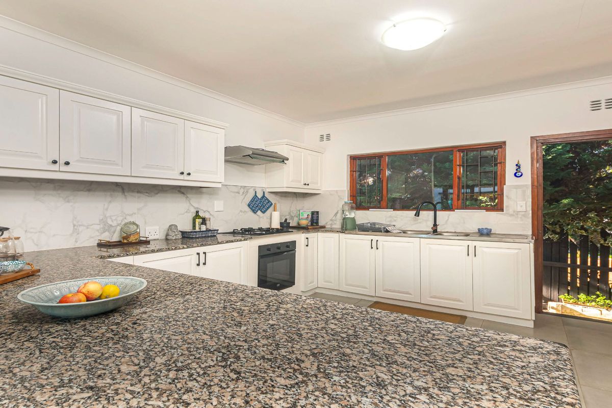 A well-maintained kitchen featuring granite countertops, white cabinetry, built-in oven, gas hob, and a marble-look splashback with direct access to the exterior.