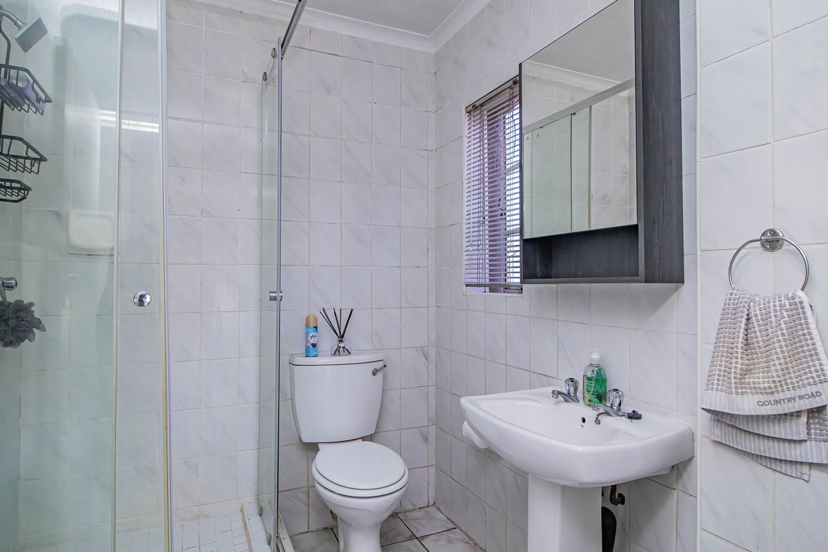 A functional bathroom featuring a glass shower enclosure, pedestal basin, toilet, and wall-mounted medicine cabinet with tiled finishes throughout.
