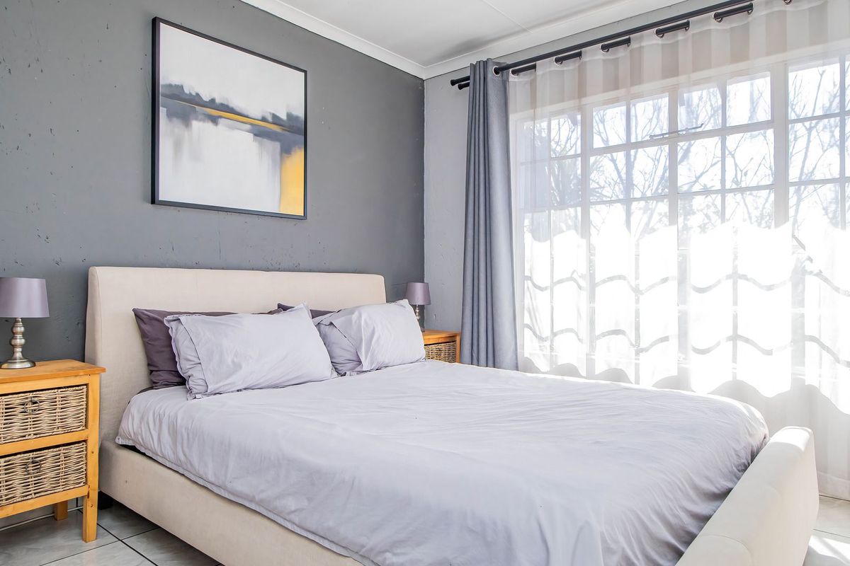 A well-lit bedroom featuring tiled flooring, a large window with curtain rails, and a grey accent wall.
