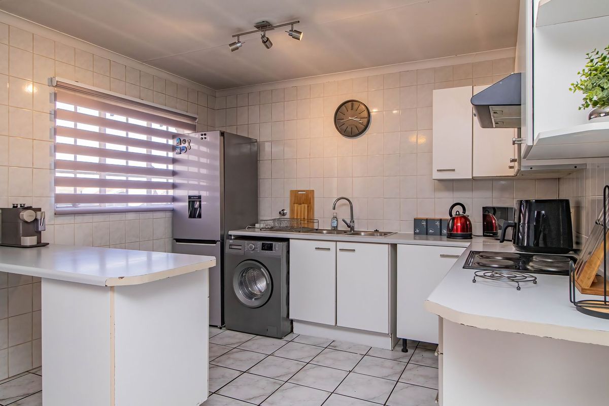 A functional kitchen featuring tiled splashbacks, built-in cabinetry, a stainless steel sink, and a built-in hob with an extractor fan.