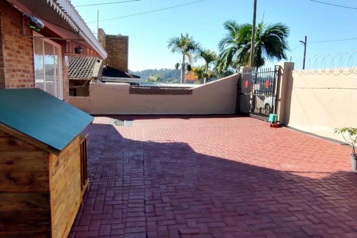 A paved rear courtyard area featuring a perimeter wall with security razor wire and a metal gate access point.