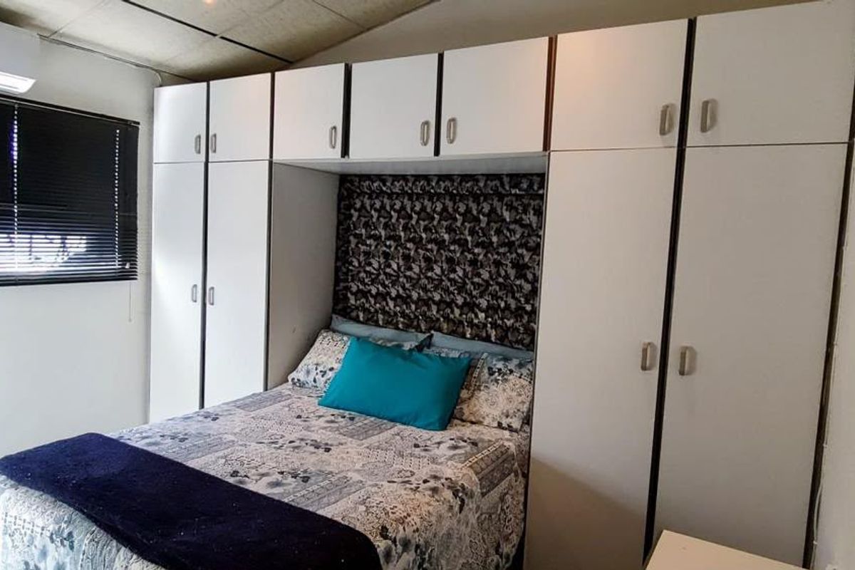 A bedroom featuring extensive built-in cabinetry surrounding the bed area, equipped with a wall-mounted air conditioning unit and window blinds.