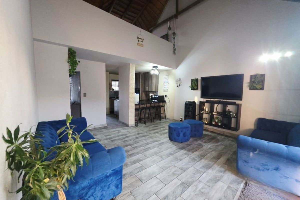 Spacious open-plan living area featuring high vaulted ceilings with exposed timber rafters, tiled flooring, and a seamless transition to the kitchen and breakfast bar.