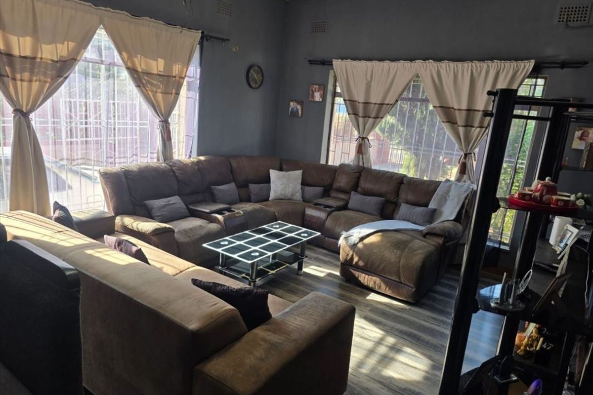 A spacious living room featuring dark grey walls, laminate flooring, and large windows fitted with security bars.