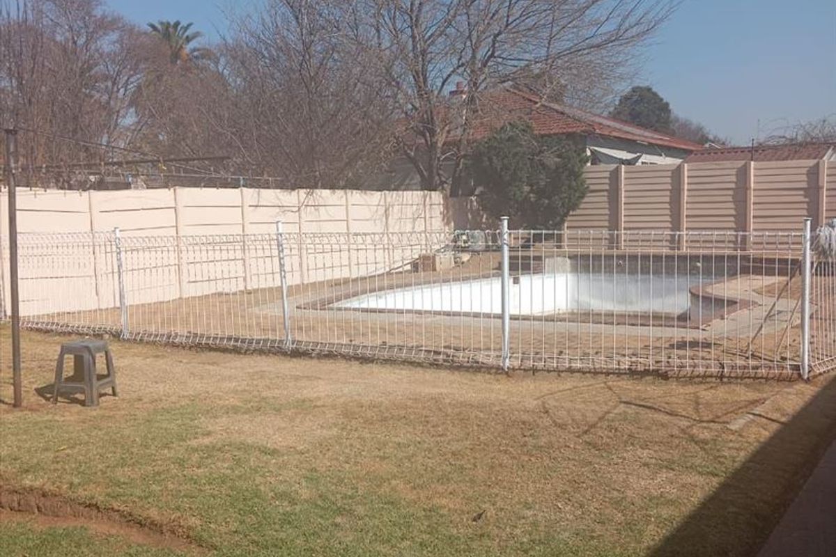 Outdoor backyard area featuring a swimming pool enclosed by metal fencing and precast concrete boundary walls.