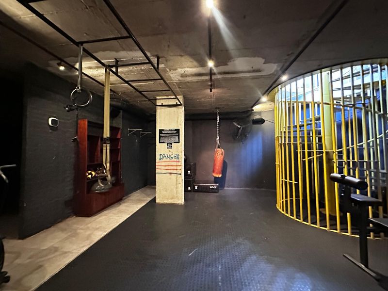 Industrial-style home gym featuring exposed concrete ceilings, rubber flooring, and a prominent yellow spiral staircase.