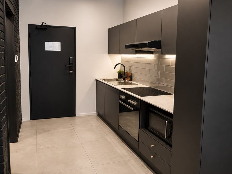 Modern kitchen featuring matte black cabinetry, stone countertops, subway tile backsplash, and integrated appliances including an oven, cooktop, and microwave.