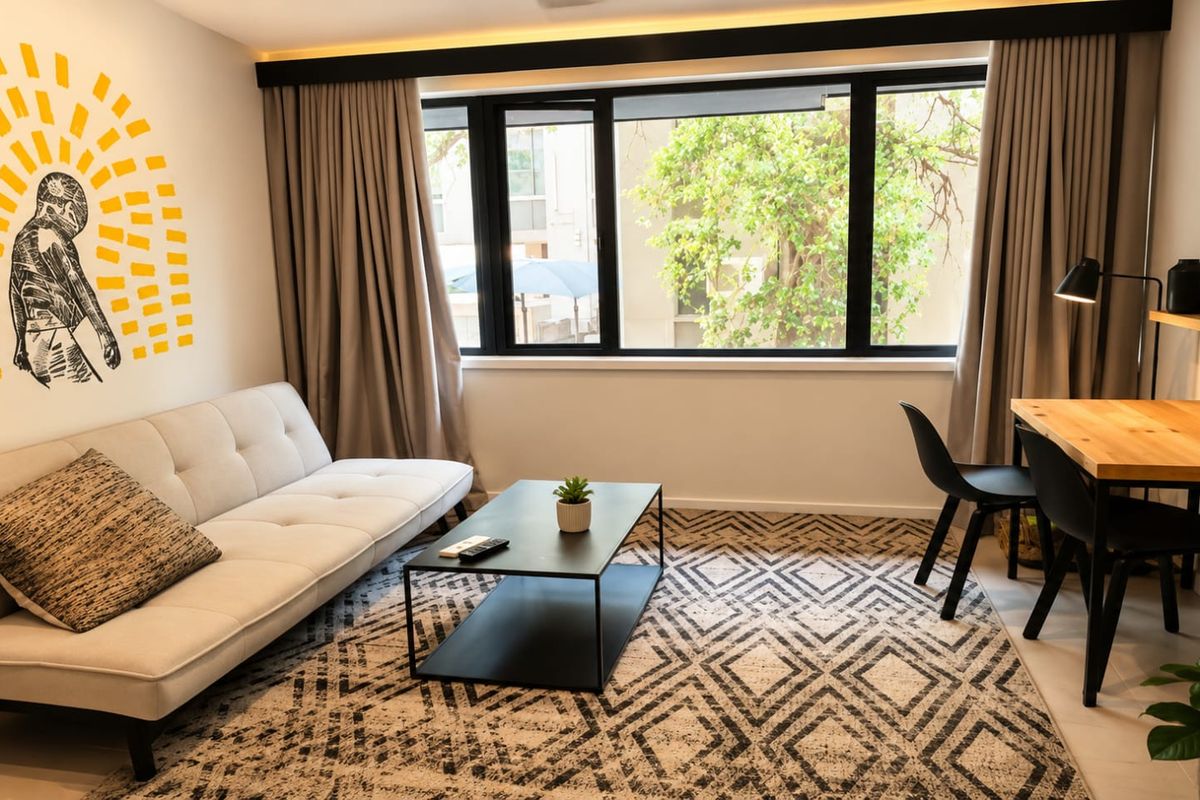 A well-lit living room featuring modern tiled flooring, recessed ceiling lighting, and a large window with black framing overlooking the exterior.