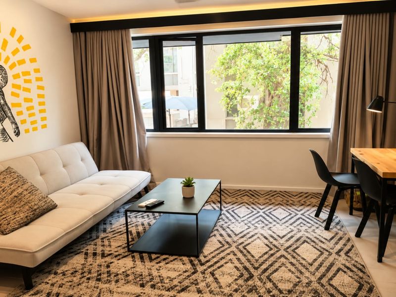 A well-lit living room featuring modern tiled flooring, recessed ceiling lighting, and a large window with black framing overlooking the exterior.