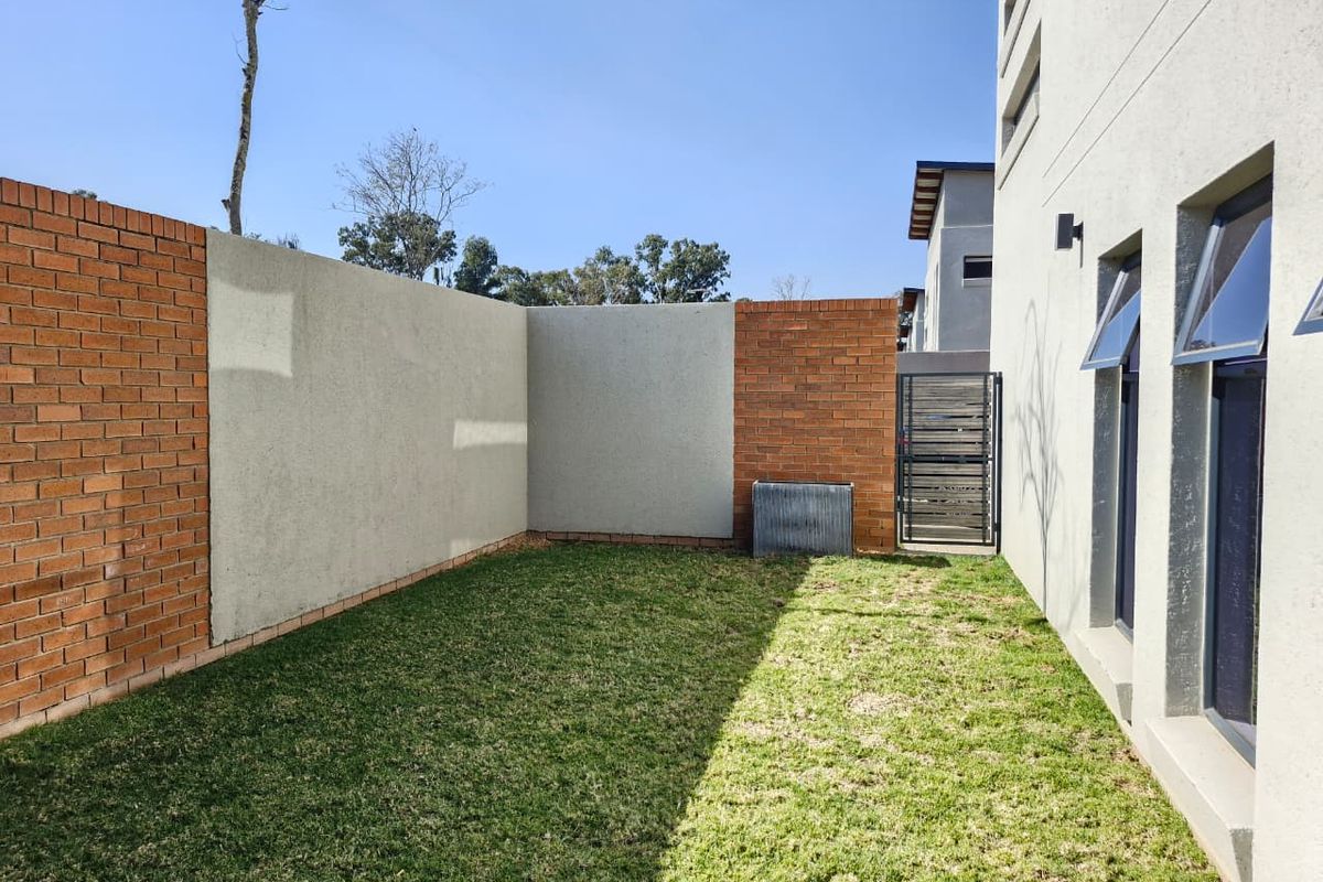 A private rear garden area featuring a combination of brick and plastered boundary walls, a small lawn, and access via a metal gate.
