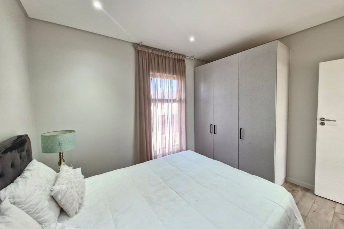A well-maintained bedroom featuring neutral tones, built-in wardrobes, recessed downlighting, and modern laminate flooring.