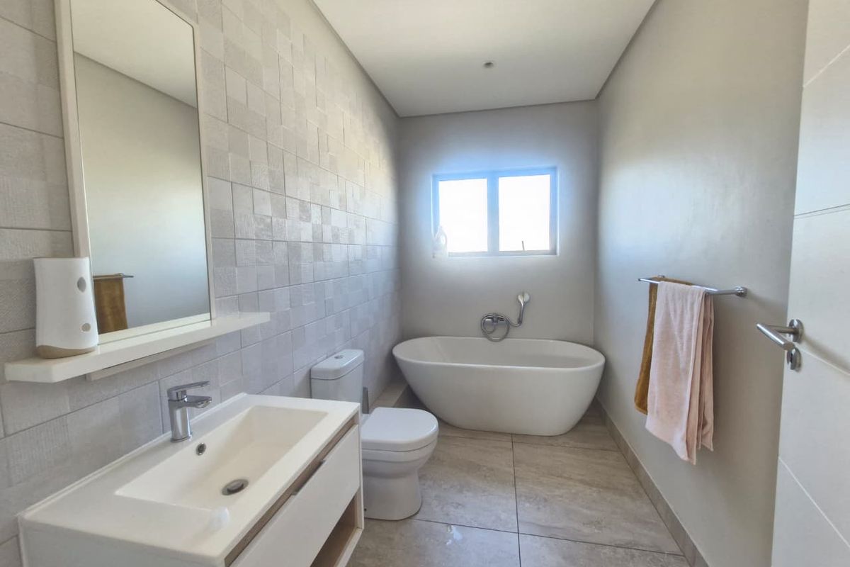 Modern bathroom featuring a sleek freestanding bathtub, wall-mounted vanity with basin, and neutral tiled finishes throughout.