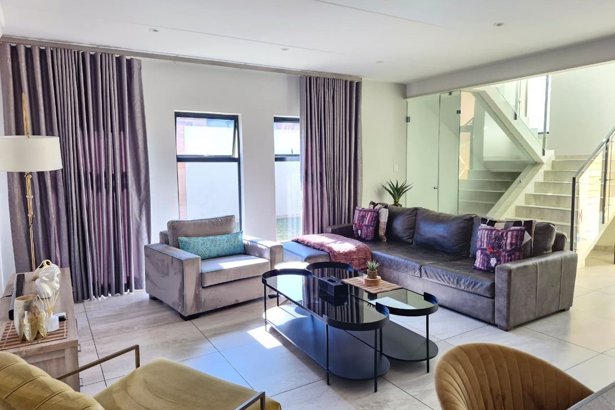 A bright and modern living room featuring large windows, tiled flooring, and a contemporary glass staircase balustrade.