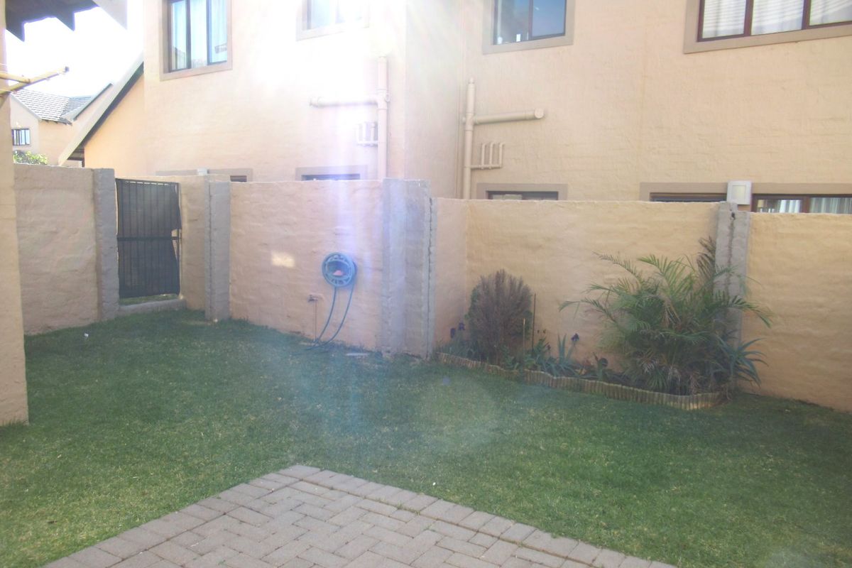A private rear garden featuring a paved patio area, a small lawn, and a secure boundary wall with a metal access gate.