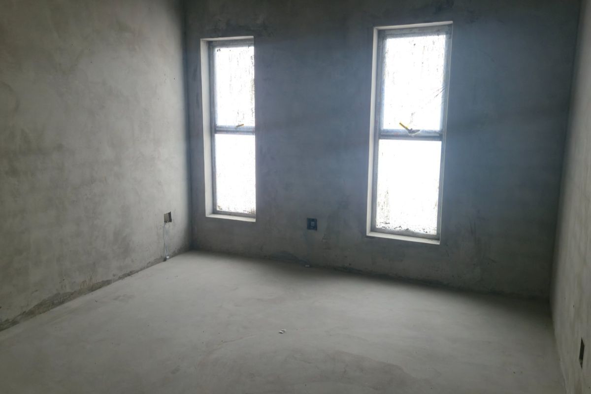 An unfinished bedroom space featuring raw concrete walls and flooring with two installed casement windows and electrical points.