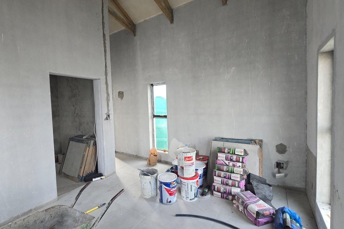 An unfinished living area featuring exposed timber rafters, tiled flooring, and raw plaster walls, currently undergoing construction and renovation.