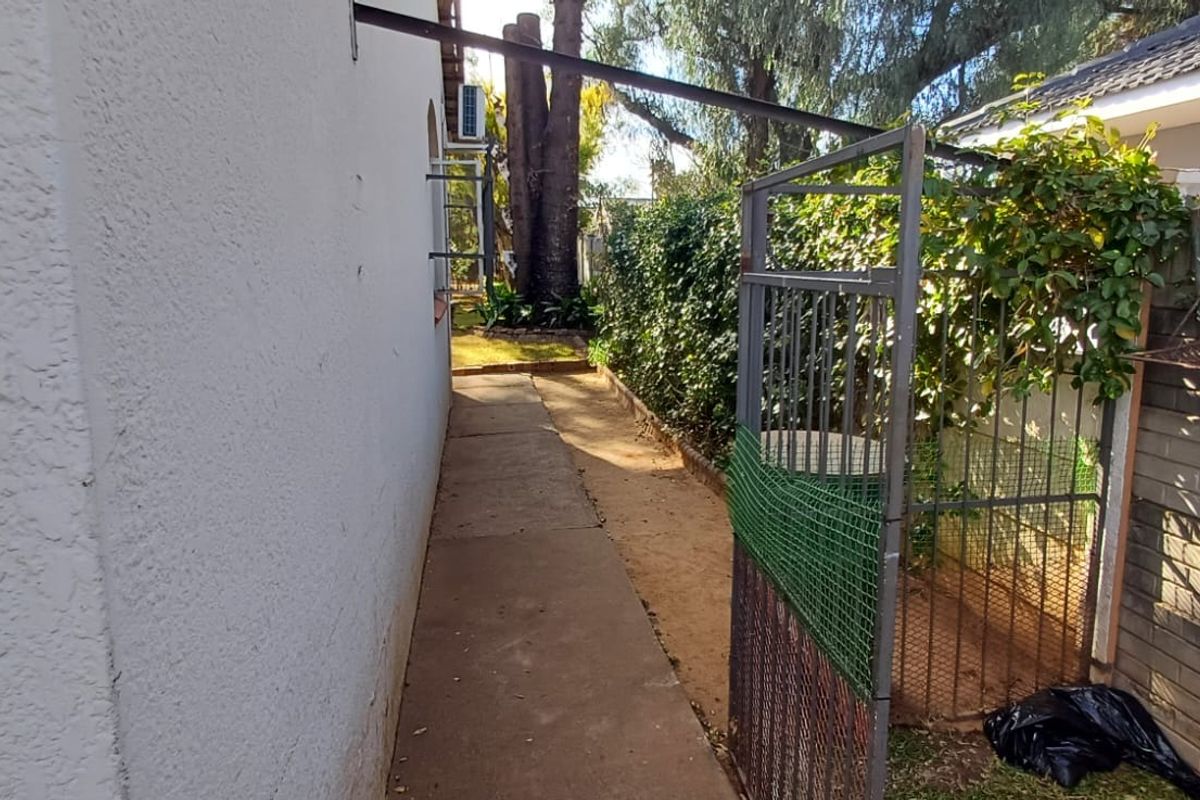 A narrow side passage featuring a concrete walkway, metal security gate, and brick boundary wall, providing access to the rear of the property.
