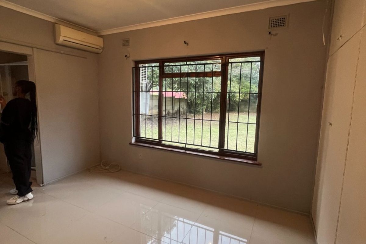 An empty bedroom featuring tiled flooring, built-in cupboards, and a split-system air conditioner, with security bars installed on the window.