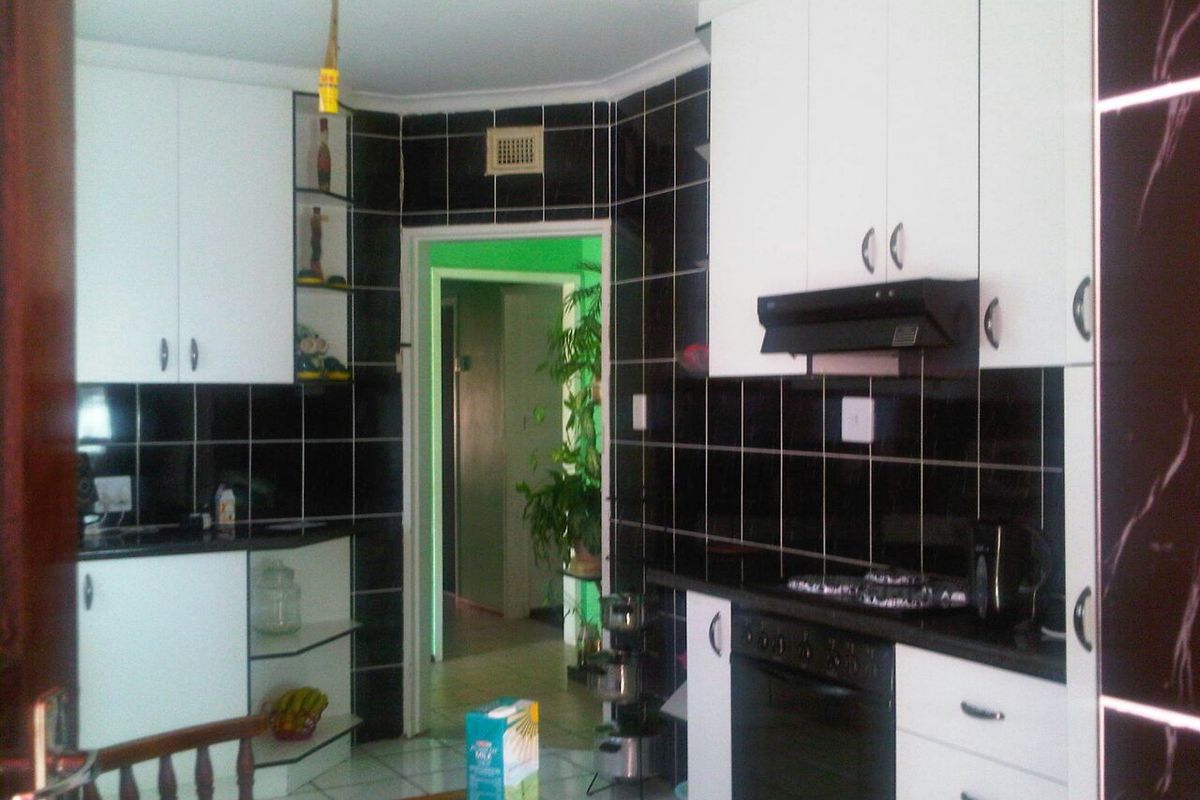 A functional kitchen featuring white cabinetry, black tiled backsplash, and built-in oven with extractor fan, leading into an adjacent hallway.