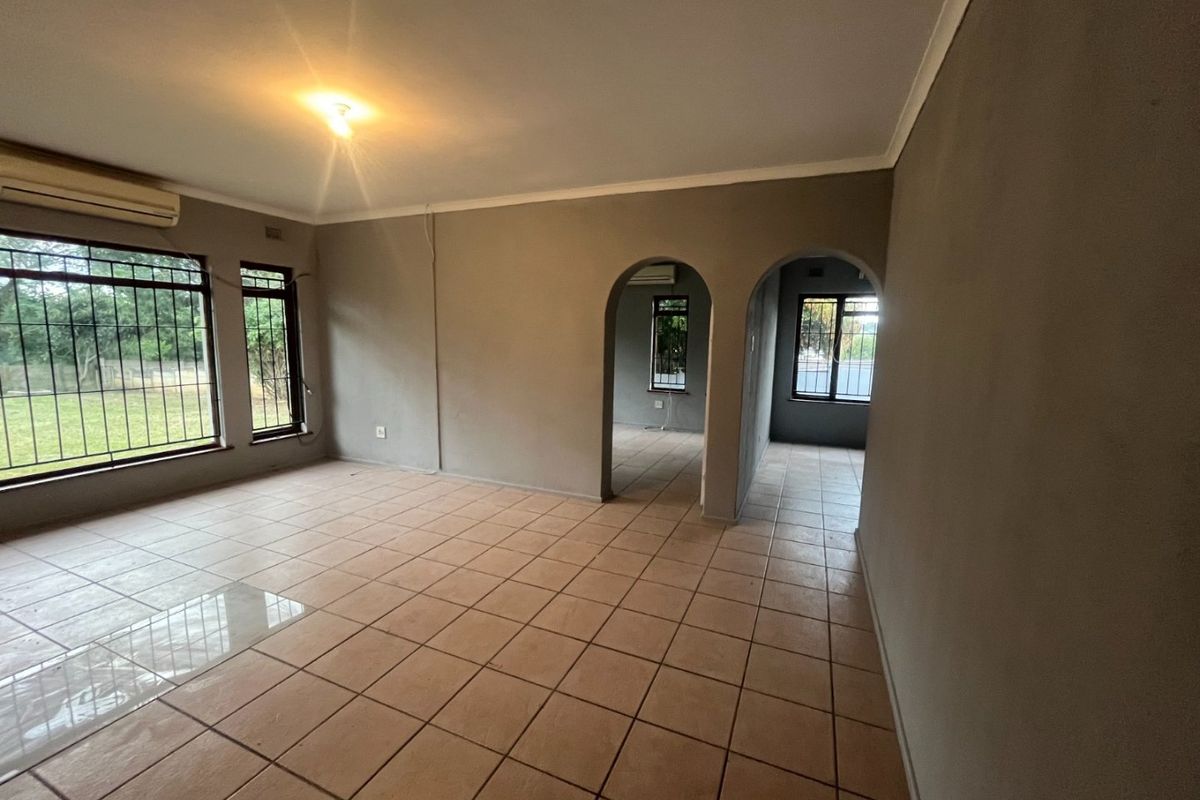 Spacious, empty living area featuring neutral walls, tiled flooring, and distinctive archways leading to adjacent rooms, complemented by built-in air conditioning.