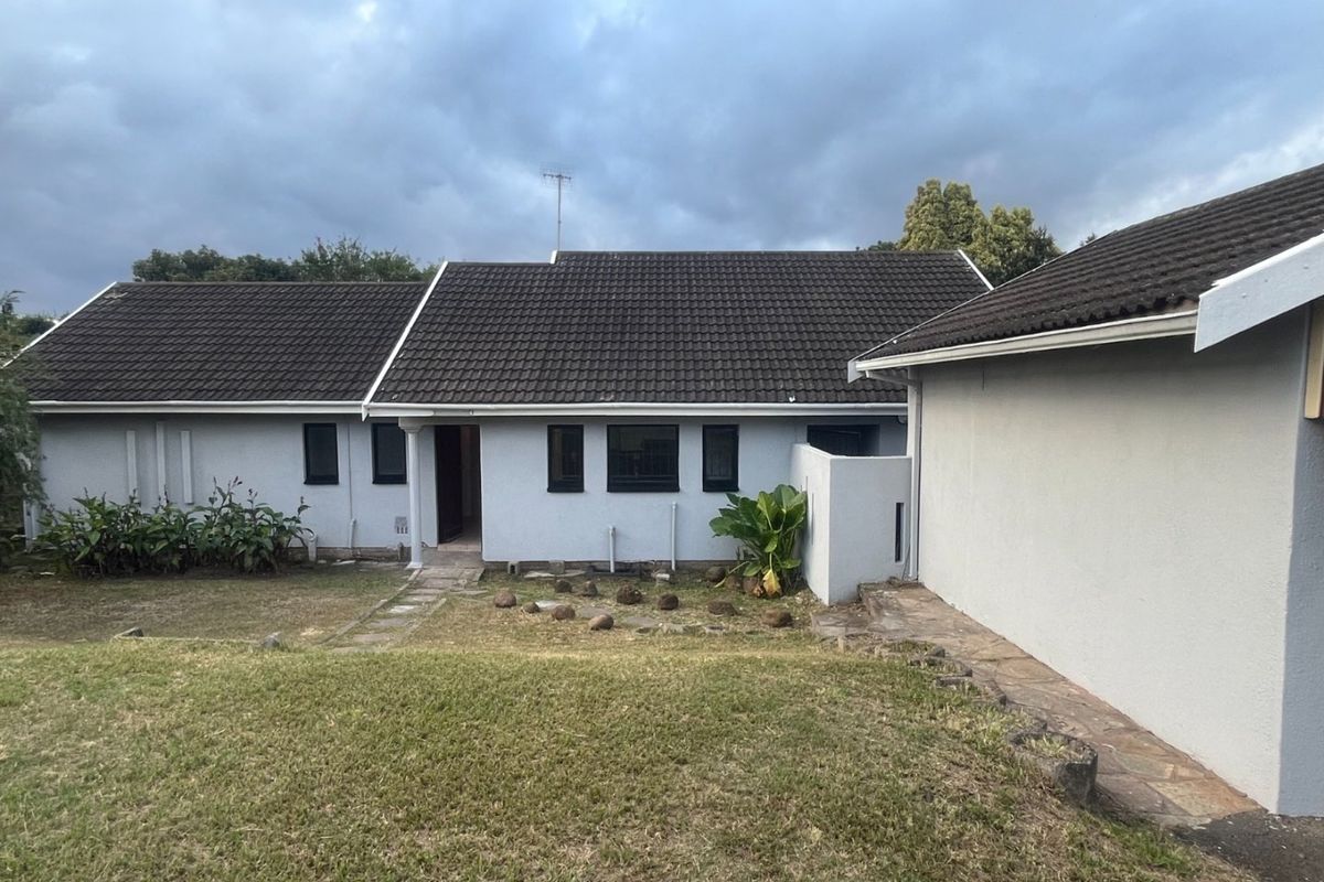 Rear view of the house featuring a tiled roof, concrete pathway, and established garden area with stone landscaping elements.