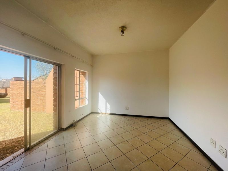 An empty, sunlit living area featuring tiled flooring and a sliding glass door providing direct access to the rear garden.
