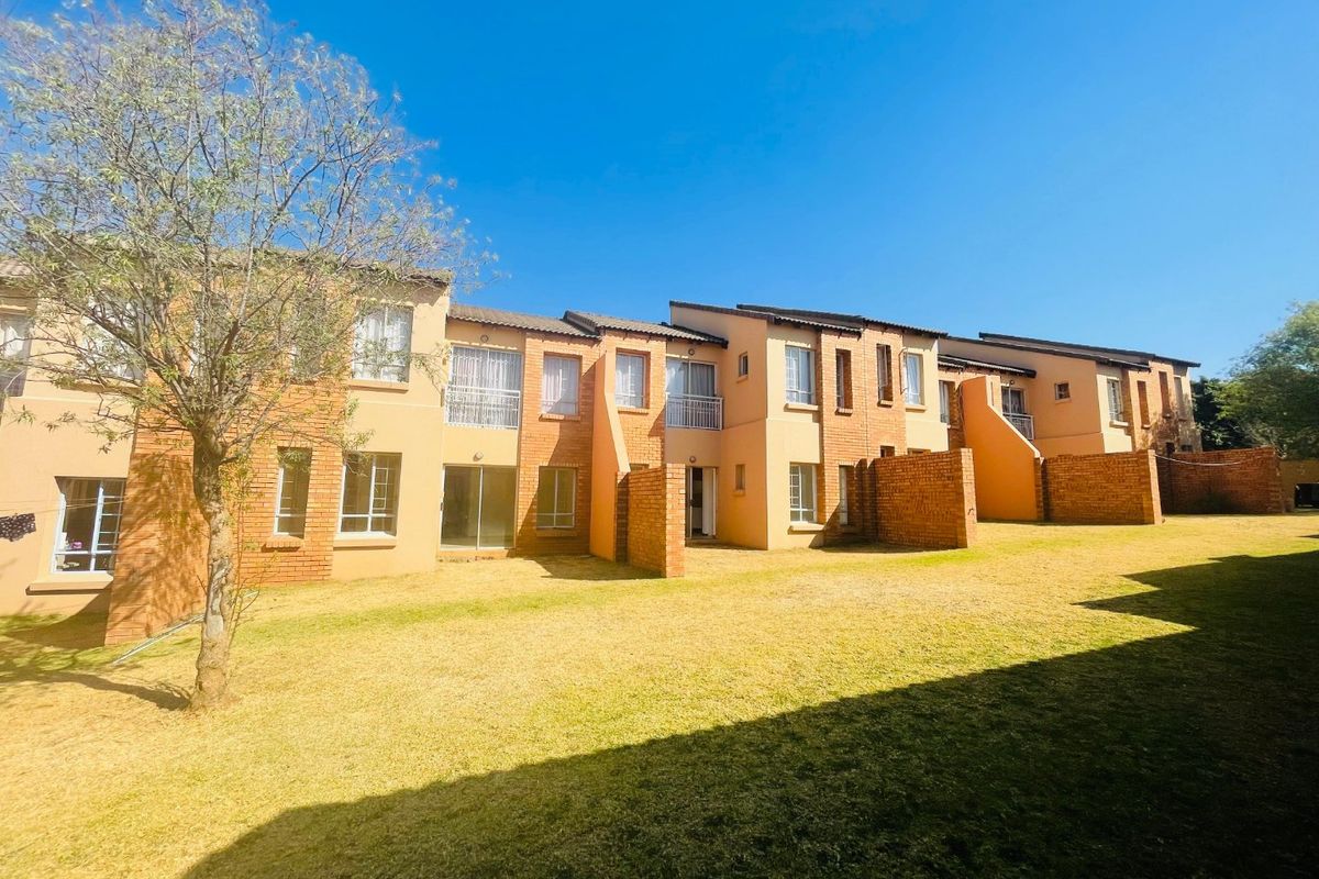 Rear view of a multi-unit apartment complex featuring brick facades, private patio areas, and a shared lawn space.