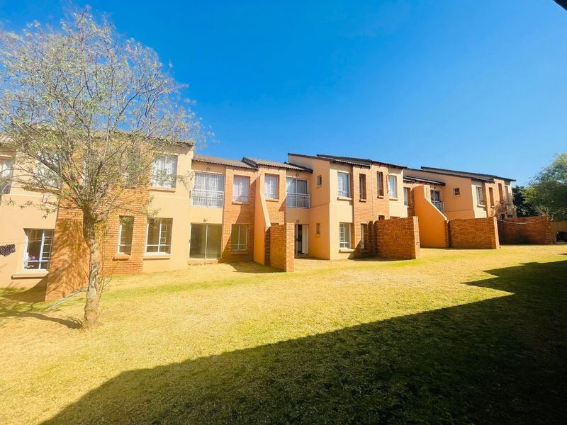 Rear view of a multi-unit apartment complex featuring brick facades, private patio areas, and a shared lawn space.