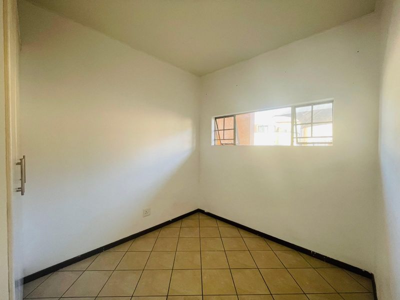 An empty bedroom featuring tiled flooring, neutral walls, and a horizontal sliding window, providing a blank canvas for interior design.