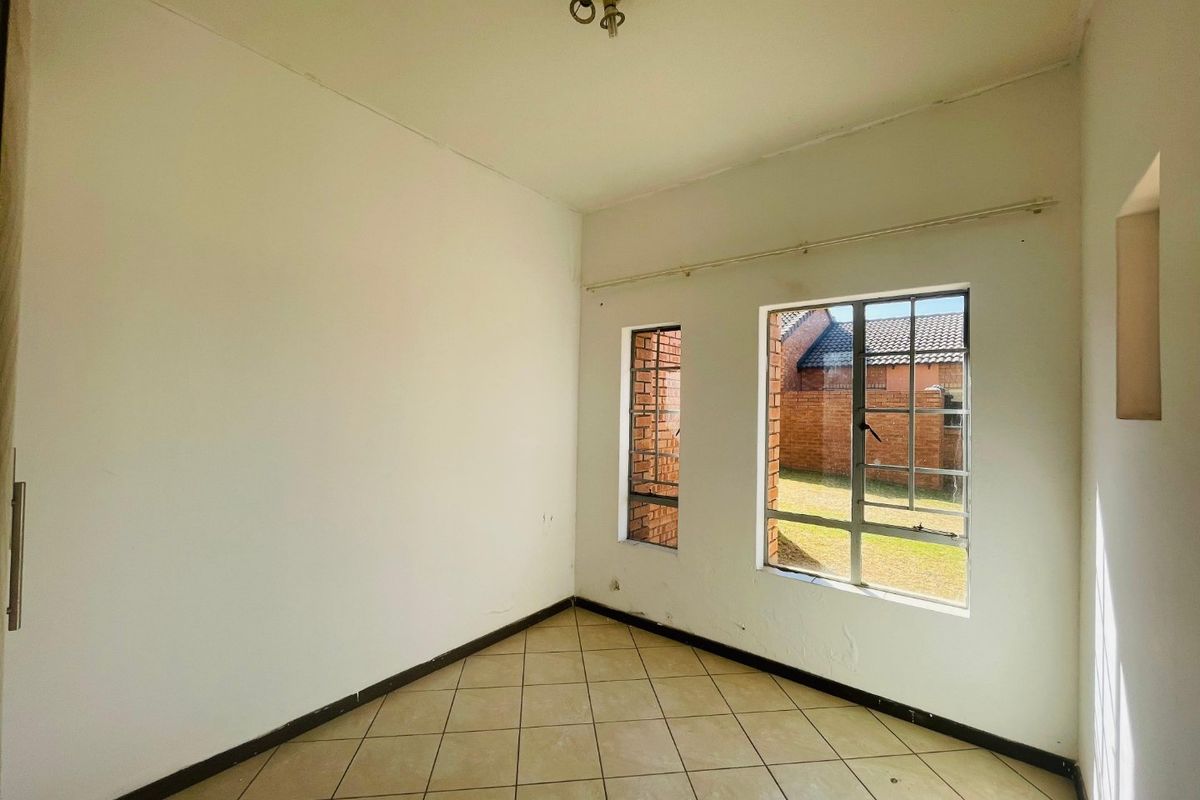 An empty bedroom featuring tiled flooring and steel-framed windows, offering a blank canvas for potential interior design and renovation.