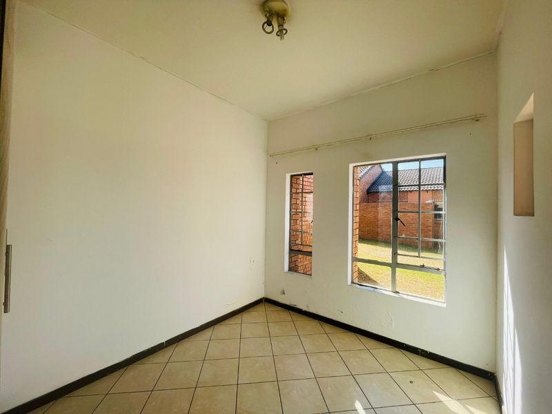 An empty bedroom featuring tiled flooring and steel-framed windows, offering a blank canvas for potential interior design and renovation.