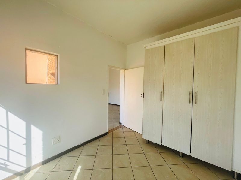 A simple bedroom featuring tiled flooring, a built-in wardrobe, and a small window, offering a clean and functional space ready for personalization.