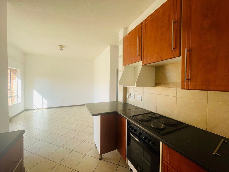 Open-plan kitchen and living area featuring wooden cabinetry, electric stove, and tiled flooring in a functional, vacant space.