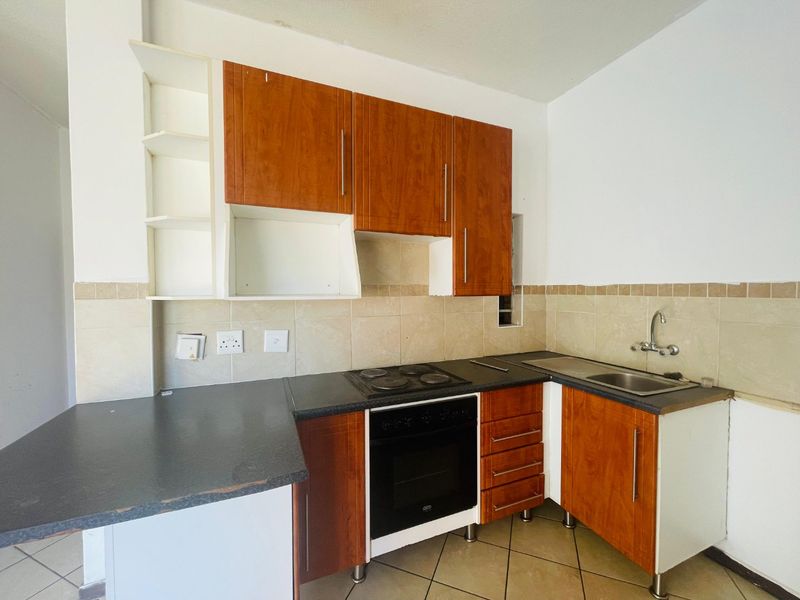 A compact kitchen featuring wood-finish cabinetry, dark laminate countertops, a built-in oven and hob, and tiled backsplash, offering a functional layout for renovation.