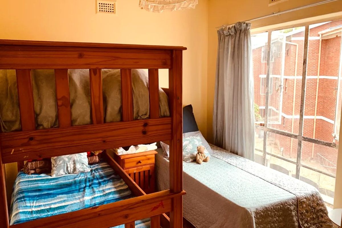 A bedroom featuring parquet flooring, a large window providing natural light, and built-in ventilation grilles.