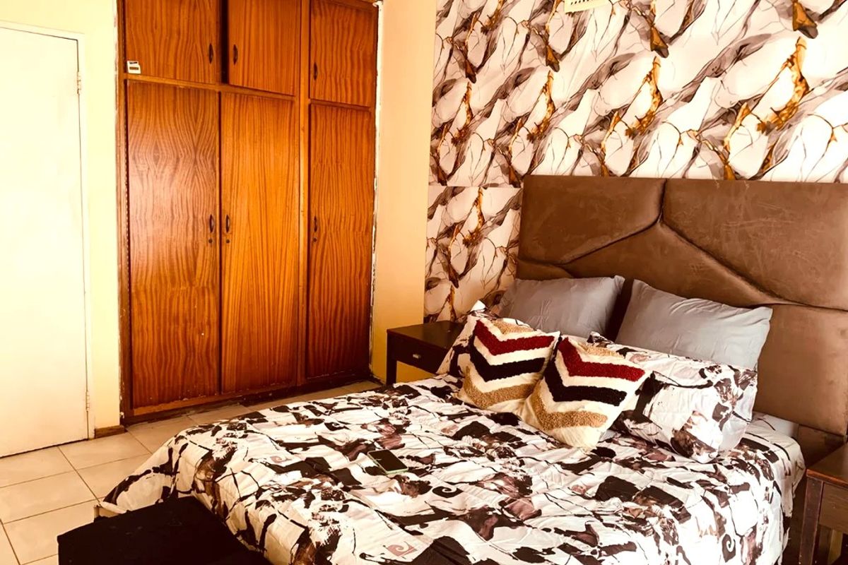 A bedroom featuring built-in wooden wardrobes, tiled flooring, and a decorative accent wall, offering functional storage and a distinct design aesthetic.