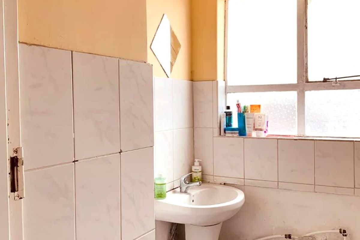 A compact bathroom featuring a pedestal washbasin, tiled splashback, and ventilation grille, currently requiring cosmetic updates and finish repairs.