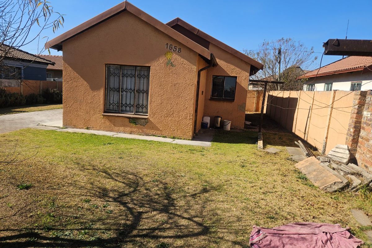 Rear view of a detached house featuring a textured facade, security bars on windows, and a surrounding perimeter wall with a small garden area.